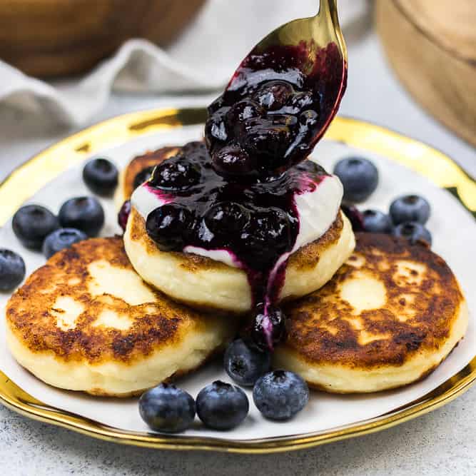 Golden syrniki cottage cheese pancakes on a plate with soured cream and berry compote