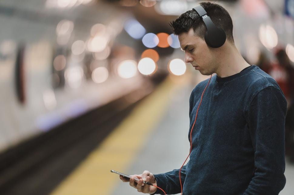 A young man in headphones looking at his phone on a metro platform